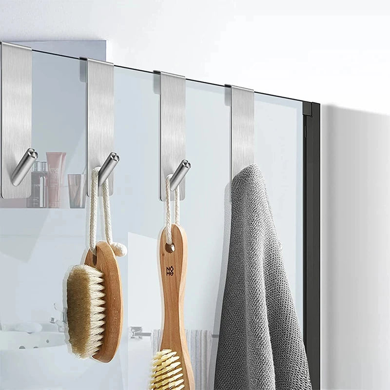 Crochets en acier inoxydable suspendus sur une paroi vitrée de douche — utilisés pour accrocher une brosse de bain et une serviette, installation sans perçage, design moderne pour salle de bain.
